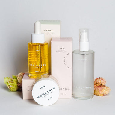 Momotaro Apotheca Tonic, Salve abd Hydrosol packagings with dried flowers over a light grey background Nudie Co