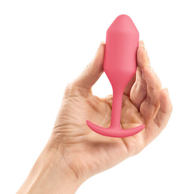 Hand holding a coral silicone weighted anal plug with torpedo shape Nudie Co