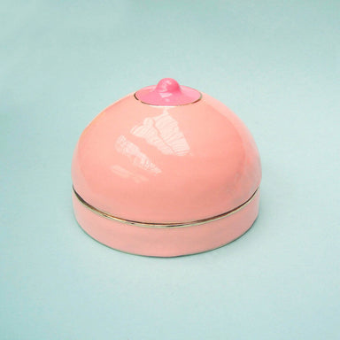 Pink breast-shaped enamel box over a light green background Nudie Co