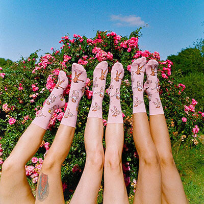 Four pairs of women's bare legs in a garden wearing socks Nudie Co
