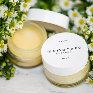 Pot of Momotaro Apotheca Salve organic vulva balm on a bed of fresh white flowers Nudie Co