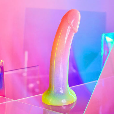 Multi-coloured gradient silicone dildo with glitter over a pink background Nudie Co