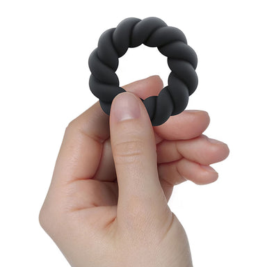 Hand holding a black textured cock ring against a white background Nudie Co