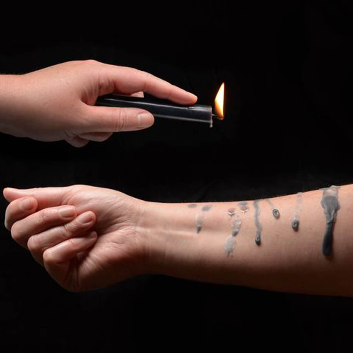 Hand holding a black wax candle dripping wax on another arm Nudie Co