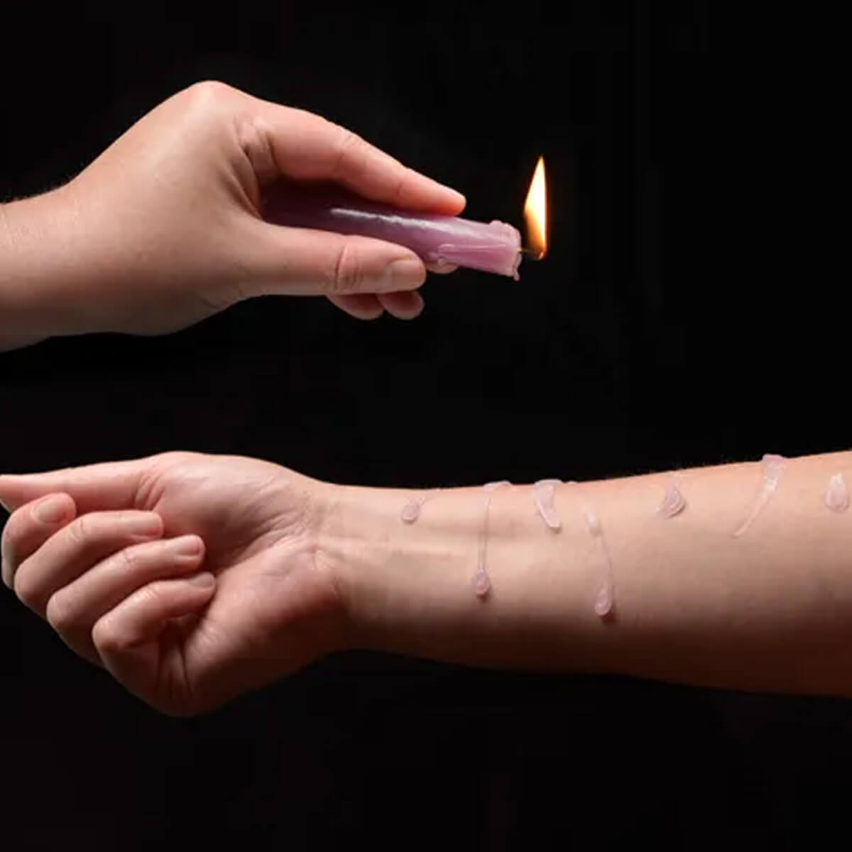 Hand holding a pink wax candle dripping wax on another arm Nudie Co