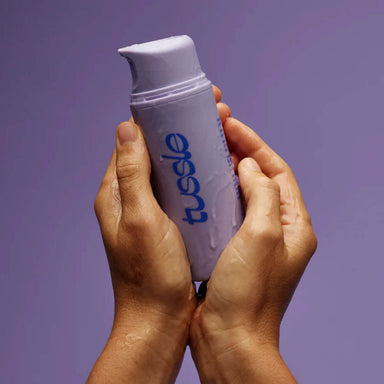 Hands holding a purple bottle with blue logo dripping with lubricant Nudie Co