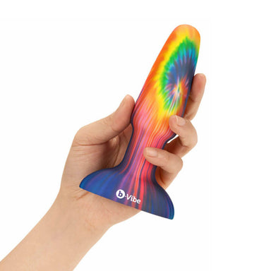 Hand holding a colourful tie-tye silicone butt plug on a white background Nudie Co
