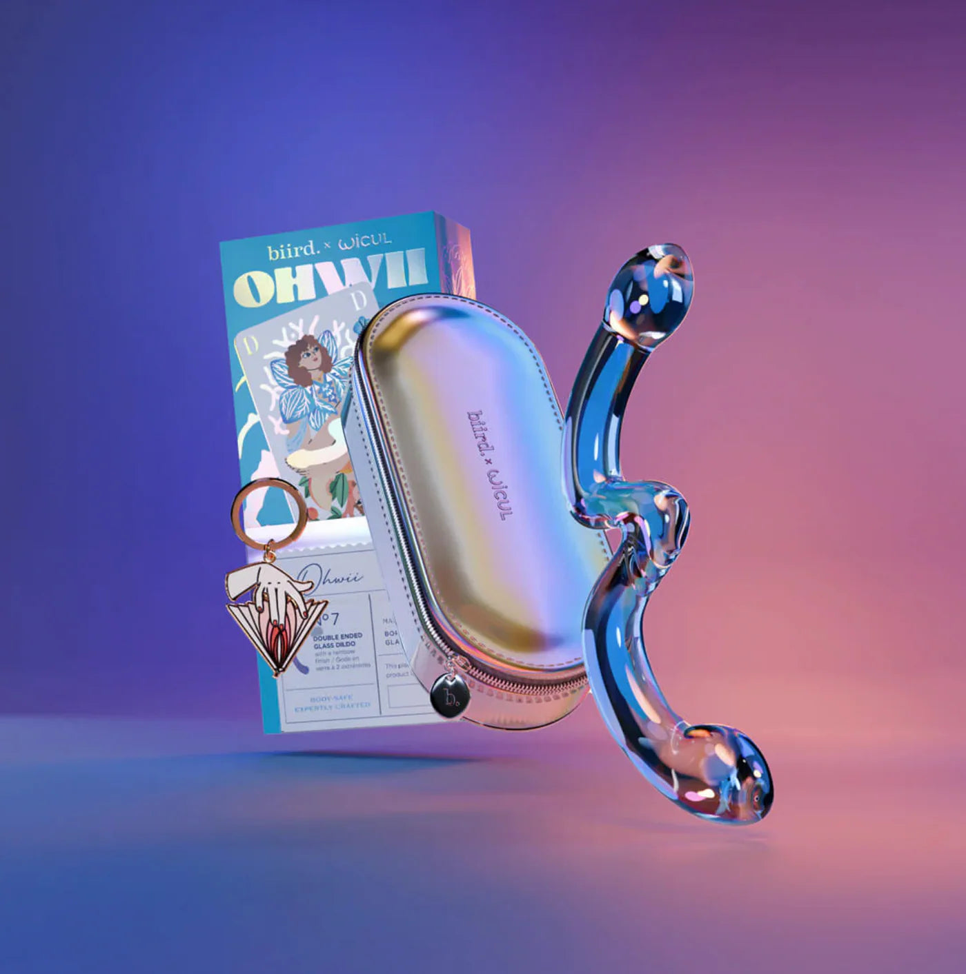 Floating double-ended glass dildo, storage case and metal keychain over a gradient blue-pink background Nudie Co