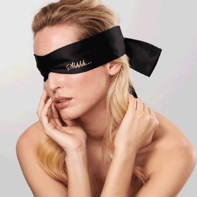 Woman wearing black satin blindfolds printed with the word 'Shhh' in gold Nudie Co