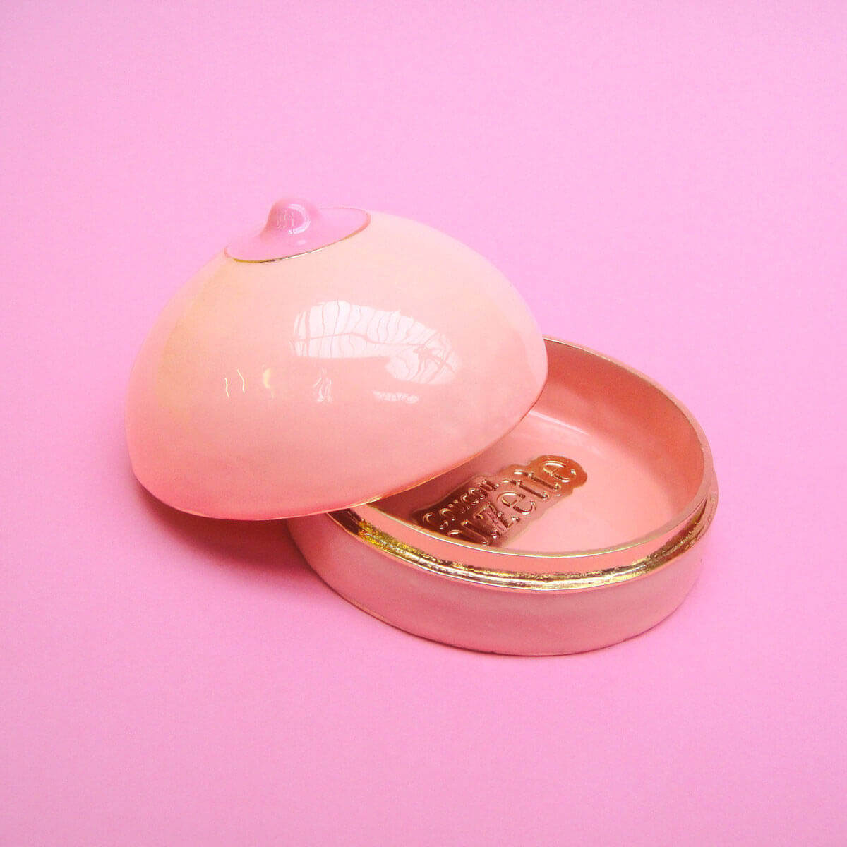 Open breast-shaped pink enamel box over a pink background Nudie Co