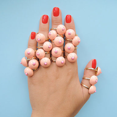 Woman's hand showing fingers covered in pink boob-shaped rings Nudie Co
