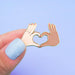 Fingers holding an enamel pin with two hands forming a love heart Nudie Co