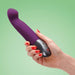 Woman's hand holding the purple Stronic G thrusting vibrator over a green background Nudie Co
