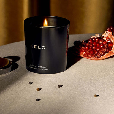 Black massage candle jar on a table with pomegranate wedge and black peppercorns Nudie Co