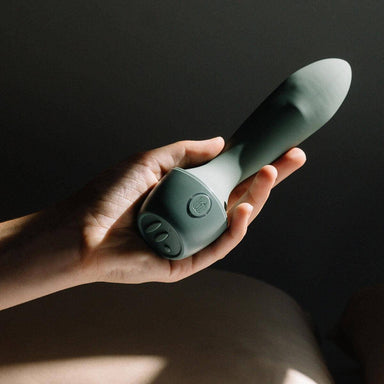 Woman's hand holding an army green G-spot vibrator with stimulating rolling bead in the shaft Nudie Co