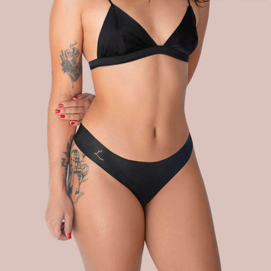 Front view of woman wearing black bra and black bikini latex underwear Nudie Co