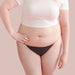 Front view of woman wearing white t-shirt and black bikini latex underwear Nudie Co