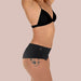 Side view of woman wearing black bra and black shortie latex underwear Nudie Co