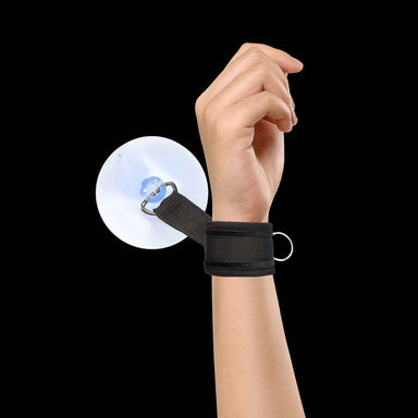 Wrist in black cuff closed with velcro strap and attached to black wall with suction cup Nudie Co