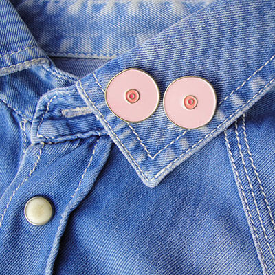 Two pink boob-shaped pins on a denim shirt's collar Nudie Co